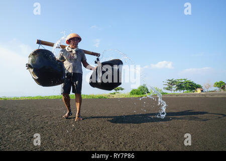 Bali Indonesien Apr 3, 2016: Traditionelle Salz Landwirt gießen Meer Wasser in schwarzen Sand als Teil des Prozesses der Herstellung von traditionellen Salz in Kusam Stockfoto