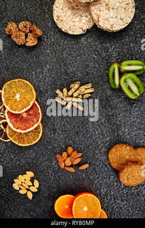 Gesunde Snacks - Sorte Hafer Müsliriegel, Reis crips, Mandel, Kiwi, getrocknete orange, auf schwarzem Hintergrund. Mix Sortiment. Ansicht von oben. Diät essen. Gluten Stockfoto