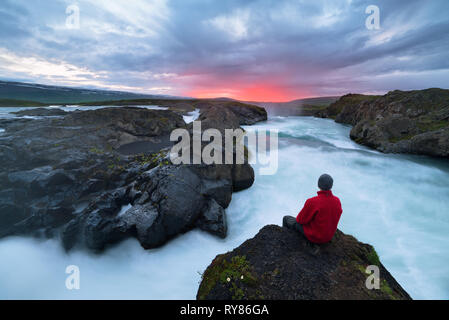 Touristische Attraktion im Norden von Island. Vor dem Wasserfall Godafoss. Skjalfandafljot Fluss in der Nähe der Stadt Akureyri. Touristische sitzt auf einem Felsen ein Stockfoto