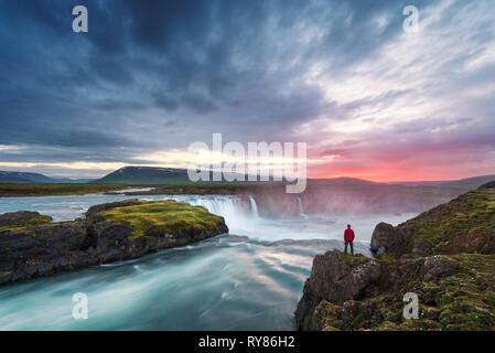 Godafoss Wasserfall. Schöne Landschaft in Island. Mann in rote Jacke, die auf dem Felsen und Suchen in der Morgendämmerung Stockfoto