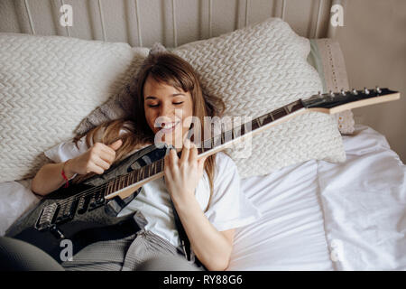 Von oben Junge Brünette Frau spielt Gitarre auf dem Bett Stockfoto