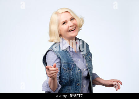 Reife Frau zeigt mit dem Finger und toothy Lächeln. Studio shot Stockfoto