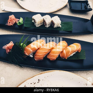 In einem Restaurant werden Gerichte mit Lachs-Sushi, Nigiri und Uramaki serviert. Japanische Küche mit Sojasauce und Wasabi - rohe Meeresfrüchte Stockfoto