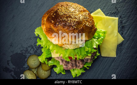 Selbstgemachte Cheeseburger mit einer Scheibe Käse und Tomaten auf einem dunklen grau Platte. Lecker und herzhaftes Burger. Stockfoto