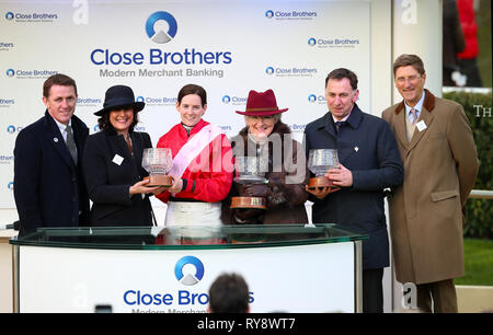 Ein P McCoy (links) stellt Jockey Rachael Blackmore (3. links) Henry de Bromhead (Zweiter von rechts) und gewinnende Verbindungen die Trophäe für das Gewinnen der Close Brothers Novizen "Handicap Chase während Meister Tag der 2019 Cheltenham Festival in Cheltenham Racecourse. Stockfoto