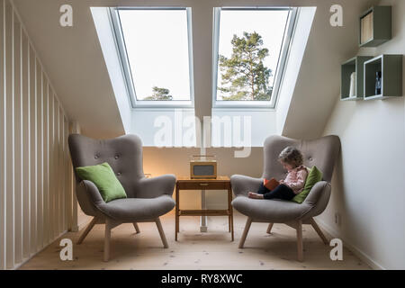 Modern Retro Design in einem Dachgeschoss/Loft. Kleine vintage Tisch mit einem Radio auf und zwei Stühlen lesen unter zwei Oberlichter mit einem kleinen Kind das Lesen einer Bo Stockfoto