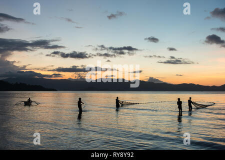 Fischer ziehen ein großes Netz aus dem Meer, den Sonnenuntergang Silhouetten in Port Barton, Palawan - Philippinen Stockfoto