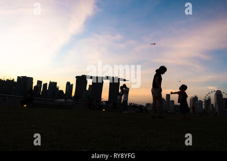 Mutter im Gespräch mit jungen Sohn im Marina Barrage, mit Singapur Skyline Sonnenuntergang Stockfoto