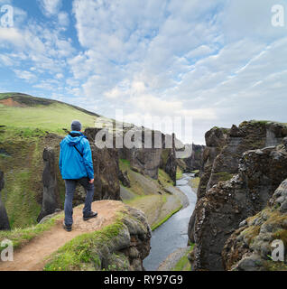 Touristen in der blauen Jacke steht auf einem Hügel. Fjadrargljufur Canyon im Südosten von Island mit dem Fjadra River fließt. Erstaunlich attracti Stockfoto