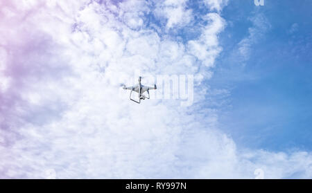 Weiß Drone Quadcopter in der Luft fliegen auf blauen Himmel mit Wolken Stockfoto