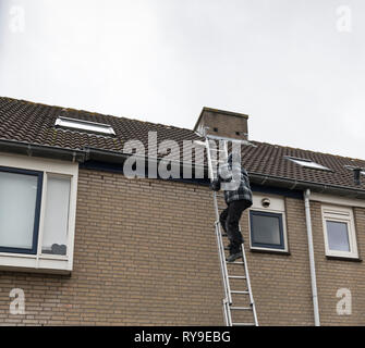 Man Klettern auf einer Leiter, Inspektion des Daches eines Hauses Stockfoto