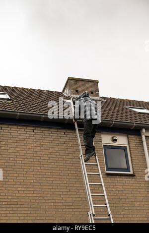 Man Klettern auf einer Leiter, Inspektion des Daches eines Hauses Stockfoto