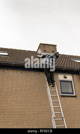 Man Klettern auf einer Leiter, Inspektion des Daches eines Hauses Stockfoto