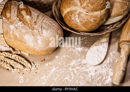 Blick auf zwei verschiedene Art von frisch gebackenem Brot auf einem urigen Hintergrund mit Weizen und Mehl. Eine Bäckerei und ein Lebensmittelgeschäft. Stockfoto