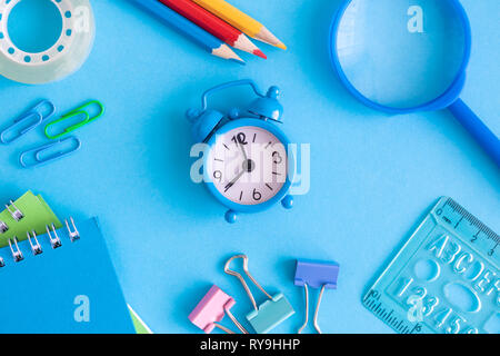 Kleine Wecker mit Schulmaterial auf blauem Hintergrund minimal Kreative zurück zu Schule Konzept. Stockfoto