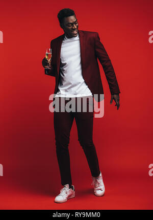Volle Länge von stattlichen jungen afrikanischen Mann tanzen mit einem Glas Champagner über den roten Hintergrund. Stockfoto