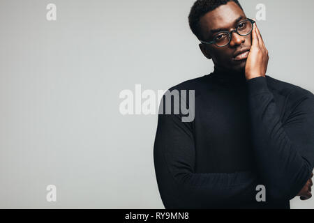 Afrikanischer Mann in casuals Denken gegen grauen Hintergrund. Nachdenklicher junger Mann im schwarzen Outfit weg schauen mit der Hand am Kinn. Stockfoto