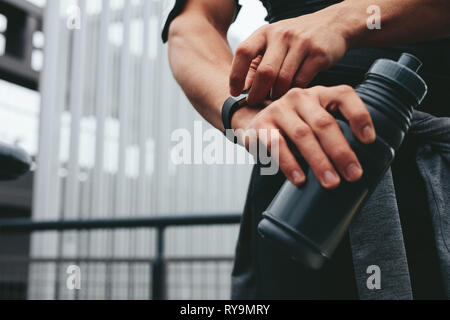 Nahaufnahme von Mann mit Wasserflasche Kontrolle seiner Performance auf Fitness App auf seine Smart Watch. Mann mit einem smartwatch seine Fortschritte zu überwachen. Stockfoto