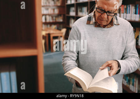 Nahaufnahme eines älteren Herrn in einer Bibliothek Blättern von Seiten eines Textes Buch. Älterer mann Kontrolle für Bücher in der Universitätsbibliothek. Stockfoto