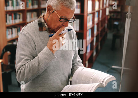 Professor an der Universität lehre in der Klasse mit einem Buch und Marker in der Hand. Älterer Mann ein Buch lesen mit Konzentration im Klassenzimmer. Stockfoto