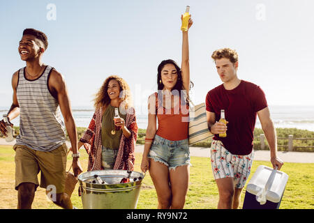 Freunde, die Kühler und trinken Whirlpool für ein Picknick am Strand. Multi-ethnischen Gruppe junger Menschen zu Fuß im Freien mit Getränken. Stockfoto