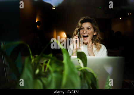 Ein Mädchen in einem Cafe mit einem Laptop funktioniert in einem gemütlichen Ort mit einer Tasse Kaffee, erhält Vergnügen. Das Konzept der freiberuflich und Arbeiten in Freude Stockfoto