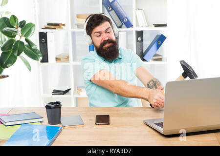 Computer lag. Gründe für Computer zurückbleiben. Wie fix langsam hinterher. Hasse office Routine. Man bärtige Kerl Kopfhörer Büro schwingen Hammer auf Comput Stockfoto