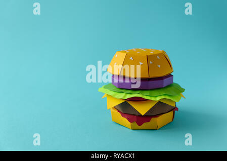 Papier Cheeseburger mit Rindfleisch, Käse, Tomaten, Salat, Zwiebel und die Sauce auf einem blauen Hintergrund. Kopieren Sie Platz. Kreative oder Kunst essen Konzept Stockfoto