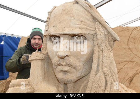 Binz, Deutschland. 12 Mär, 2019. Der Bildhauer Bagrat Stepanayan aus Russland arbeitet auf dem Sand Skulptur Johnny Depp als Captain Jack Sparrow in einer Szene des Films "Fluch der Karibik" auf dem Gelände der Sandskulpturenfestival. Künstlerinnen und Künstler aus verschiedenen europäischen Ländern werden derzeit erstellen 45 riesige Zahlen für die 10 Sand Skulptur zeigen im Ostseebad Binz. Der Sand Skulpturen zeigen, eröffnet am 16.03.2018. Quelle: Stefan Sauer/dpa-Zentralbild/dpa/Alamy leben Nachrichten Stockfoto