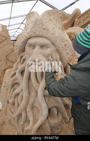 Binz, Deutschland. 12 Mär, 2019. Der Bildhauer Bagrat Stepanayan aus Russland arbeitet auf dem Sand Skulptur Captain Barbossa in einer Szene des Films "Fluch der Karibik" mit dem Film Davy Jones auf dem Gelände der Sandskulpturenfestival. Künstlerinnen und Künstler aus verschiedenen europäischen Ländern werden derzeit erstellen 45 riesige Zahlen für die 10 Sand Skulptur zeigen im Ostseebad Binz. Der Sand Skulpturen zeigen, eröffnet am 16.03.2018. Quelle: Stefan Sauer/dpa-Zentralbild/dpa/Alamy leben Nachrichten Stockfoto