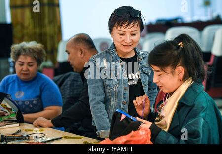 (190313)---- HAMI, März 13, 2019 (Xinhua) - Renagul (2. R) bespricht Sticktechniken mit aygul Iskender (1. R) in Ihrer Werkstatt in Yizhou Bezirk von Hami Stadt im Nordwesten Chinas Autonome Region Xinjiang Uygur, am 8. März 2019. Die Haute Couture, buchstäblich mit dem Namen 'blühende Blume', mit handgemachter Stickerei mit ausgeprägten lokalen Stil gestaltet, war auf der Modewoche in Paris 2016 präsentiert. Dies änderte sich sticken Renagul's Leben, der nie dachte, dass ihre Werke in einer Welt displaed sein würde - berühmte Fashion Show. Renagul wuchs in einer Stickerei Familie in Hami. Beeinflusst von h Stockfoto