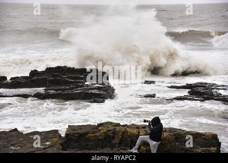 Porthcawl, in Bridgend, Südwales. 13. Mär 2019. UK Wetter: Eine gelbe Wetter Warnung bleibt für viel von Großbritannien heute als Sturm Gareth sich quer durch das Land. Sturm Gareths starke Stürme und Starkregen haben, wodurch Unterbrechungen, mit Schiene und Straße links. Bilder zeigen die Szene in Porthcawl, in Bridgend, Südwales, heute Morgen. Mit dem Leuchtturm von riesigen Wellen von Sturm Gareth getroffen. Fotografen sind abgebildet, die auf Felsen thront als Wellen kommen an Land abstürzt. Stockfoto