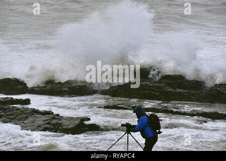 Porthcawl, in Bridgend, Südwales. 13. Mär 2019. UK Wetter: Eine gelbe Wetter Warnung bleibt für viel von Großbritannien heute als Sturm Gareth sich quer durch das Land. Sturm Gareths starke Stürme und Starkregen haben, wodurch Unterbrechungen, mit Schiene und Straße links. Bilder zeigen die Szene in Porthcawl, in Bridgend, Südwales, heute Morgen. Mit dem Leuchtturm von riesigen Wellen von Sturm Gareth getroffen. Fotografen sind abgebildet, die auf Felsen thront als Wellen kommen an Land abstürzt. Stockfoto