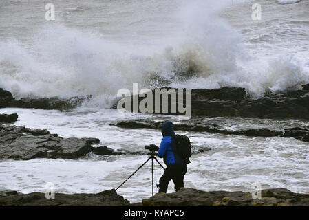 Porthcawl, in Bridgend, Südwales. 13. Mär 2019. UK Wetter: Eine gelbe Wetter Warnung bleibt für viel von Großbritannien heute als Sturm Gareth sich quer durch das Land. Sturm Gareths starke Stürme und Starkregen haben, wodurch Unterbrechungen, mit Schiene und Straße links. Bilder zeigen die Szene in Porthcawl, in Bridgend, Südwales, heute Morgen. Mit dem Leuchtturm von riesigen Wellen von Sturm Gareth getroffen. Fotografen sind abgebildet, die auf Felsen thront als Wellen kommen an Land abstürzt. Stockfoto