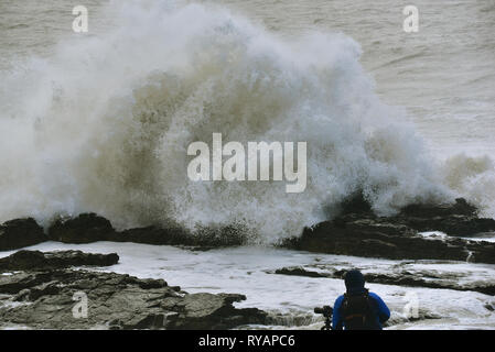 Porthcawl, in Bridgend, Südwales. 13. Mär 2019. UK Wetter: Eine gelbe Wetter Warnung bleibt für viel von Großbritannien heute als Sturm Gareth sich quer durch das Land. Sturm Gareths starke Stürme und Starkregen haben, wodurch Unterbrechungen, mit Schiene und Straße links. Bilder zeigen die Szene in Porthcawl, in Bridgend, Südwales, heute Morgen. Mit dem Leuchtturm von riesigen Wellen von Sturm Gareth getroffen. Fotografen sind abgebildet, die auf Felsen thront als Wellen kommen an Land abstürzt. Stockfoto