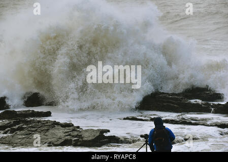 Porthcawl, in Bridgend, Südwales. 13. Mär 2019. UK Wetter: Eine gelbe Wetter Warnung bleibt für viel von Großbritannien heute als Sturm Gareth sich quer durch das Land. Sturm Gareths starke Stürme und Starkregen haben, wodurch Unterbrechungen, mit Schiene und Straße links. Bilder zeigen die Szene in Porthcawl, in Bridgend, Südwales, heute Morgen. Mit dem Leuchtturm von riesigen Wellen von Sturm Gareth getroffen. Fotografen sind abgebildet, die auf Felsen thront als Wellen kommen an Land abstürzt. Stockfoto