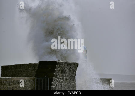 Porthcawl, in Bridgend, Südwales. 13. Mär 2019. UK Wetter: Eine gelbe Wetter Warnung bleibt für viel von Großbritannien heute als Sturm Gareth sich quer durch das Land. Sturm Gareths starke Stürme und Starkregen haben, wodurch Unterbrechungen, mit Schiene und Straße links. Bilder zeigen die Szene in Porthcawl, in Bridgend, Südwales, heute Morgen. Mit dem Leuchtturm von riesigen Wellen von Sturm Gareth getroffen. Fotografen sind abgebildet, die auf Felsen thront als Wellen kommen an Land abstürzt. Stockfoto