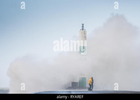 Aberystwyth, Großbritannien. 13 Mär, 2019. UK Wetter: Junge Männer Gefahren nehmen dramatische Fotos von sich selbst in der Nähe der Wellen als Gale force Winds aus Sturm Gareth - der dritte namens Sturm von 2019 - Aberystwyth auf der Cardigan Bay Küste treffen, West Wales UK am Mittwoch Nachmittag. Böen von bis zu 70 oder 80 mph sind in exponierten nördlichen Regionen Prognose, mit der Gefahr von schweren Sachschäden und erheblichen Betriebsunterbrechungen zu reisen und Power Services Photo Credit: Keith Morris/Alamy leben Nachrichten Stockfoto