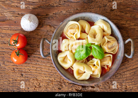 Tortellini auf Holz mit Tomatensauce. Stockfoto