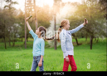 Zwei lustige kleine Mädchen mit angeschlossenen Haar unter selfie Foto mit Handy in Spring Green Park Outdoor Freizeitaktivitäten Stockfoto