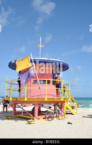 Bunt bemalte Art Deco lifeguard Station an sonnigen South Beach mit Gelb und Lila surf alert Flaggen im Wind, Miami, Florida, USA Stockfoto