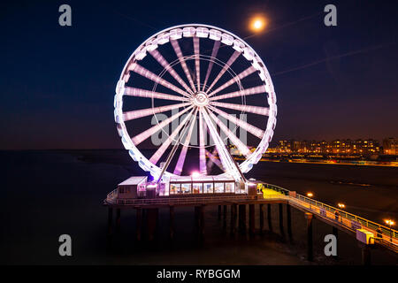 Beleuchtetes Riesenrad auf dem Pier in der Nacht im Mondlicht. Scheveningen, Den Haag auf dem Hintergrund, beliebtes touristisches Reiseziel. Stockfoto