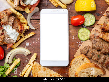 Gyros Pita, Shawarma, online bestellen. Zwei pita Brot Wraps mit Fleisch, und leerer Bildschirm Mobiltelefon auf Holztisch, Platz für Text Stockfoto