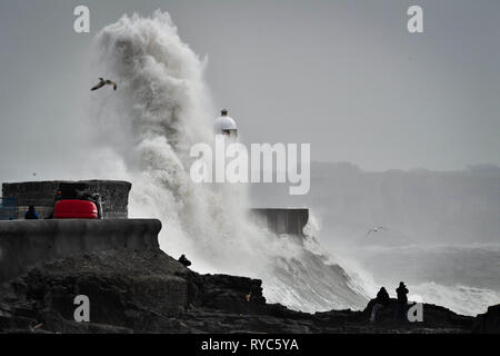 Riesige Wellen schlagen gegen die hafenmauer als Zuschauer von den Felsen aus sehen Sie in das Meer bei Porthcawl, Wales, in dem starke Regenfälle und starke Winde verursacht haben Reisen Störungen in einigen Teilen des Vereinigten Königreichs als Sturm Gareth Osten bewegt. Stockfoto