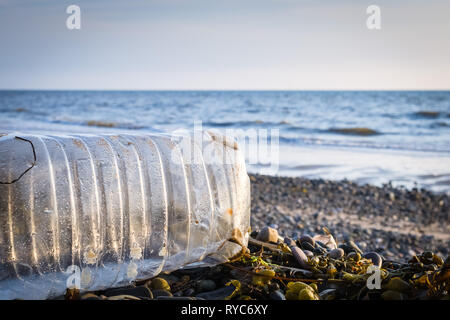 Ein angeschwemmten Plastikflaschen und Algen auf einem Kieselstrand mit dem Meer im Hintergrund und eine niedrige Sonne Stockfoto