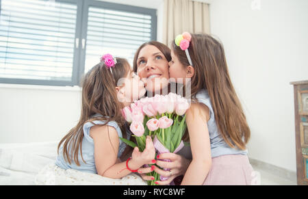Happy Mother's Day Konzept. Kleinen Töchtern Zwillinge Kuss ihre Mutter mit einem Tulip Bouquet. Stockfoto