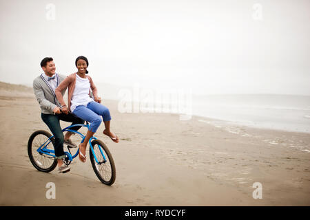 Lächelnd junges Paar mit dem Fahrrad entlang der Strand bei Ebbe. Stockfoto