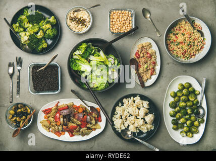Veganen Abendessen oder Mittagessen Tabelle einstellen. Verschiedene gesunde vegetarische Gerichte in Platten und Schüsseln auf konkrete Tabelle. Flachbild-lay von frischen und gekochtes Gemüse s Stockfoto