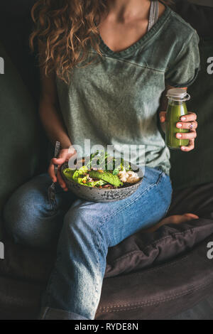 Gesundes Mittag- oder Abendessen. Frau in T-Shirt und Jeans sitzen und halten vegan Superbowl oder Buddha Schüssel mit Hummus, Gemüse, Salat, Bohnen, Couscous Stockfoto