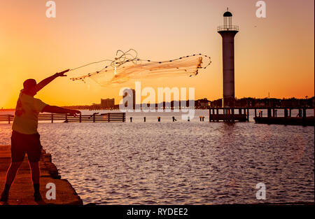 Ein Mann wirft einen Brill net im Broadwater Beach Marina als die Sonne auf Leuchtturm der Marina, 24.02.2019, in Biloxi, Mississippi. Stockfoto